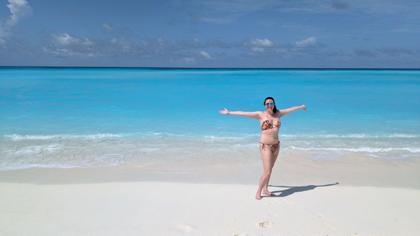 Libby stands on the beach at fulhadhoo with arms outstretched 
